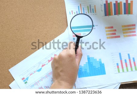 Hand holding a magnifying glass on a sheet and chart