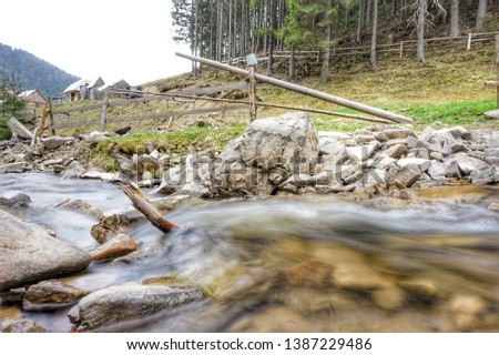 Mountain stream in the forest, at the bottom are stones. Near pasture fence for livestock.