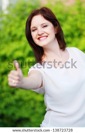 Portrait of young beautiful woman showing thumbs up at summer green park