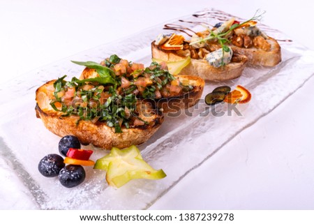 Tasty savory tomato Italian appetizers, or bruschetta, on slices of toasted baguette garnished with basil, close-up on a white background.