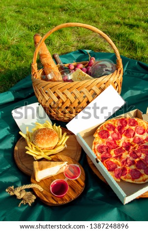
outdoor food near the water, a basket of wine and cheese, two groceries, a tablecloth with food
