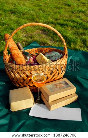 
outdoor food near the water, a basket of wine and cheese, two groceries, a tablecloth with food