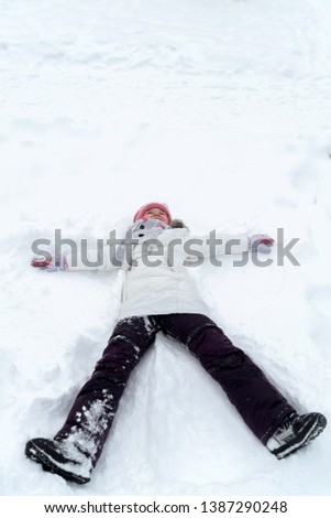 Girl lying on the snow with arms outstretched to the sides