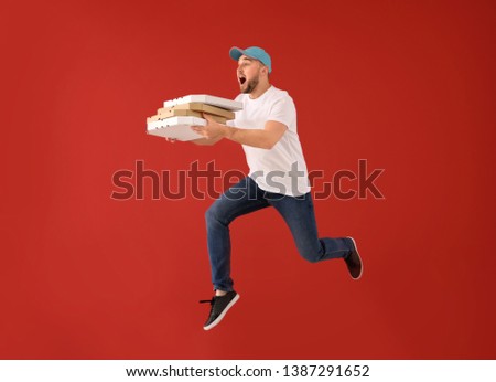Jumping male courier with pizza boxes on color background