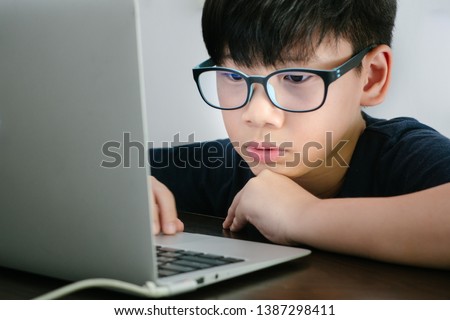 An asian preteen (tween) boy wearing Blue Light Blocking Glasses while coding with his laptop to protect his eyes from eyes problem. Computer Vision Syndrome: KIDS health, dry eyes concern - Close up Royalty-Free Stock Photo #1387298411