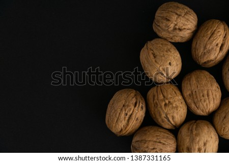 Walnuts in the shell lying on black surface, top view. Background of round walnuts. Healthy nuts and seeds composition.