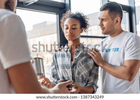 handsome volunteer hugging african american woman taking canned food in charity center