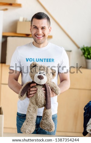 good-looking, smiling volunteer holding teddy bear and looking at camera 