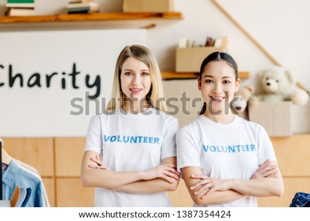 two beautiful multicultural volunteer girls with crossed arms smiling and looking at camera