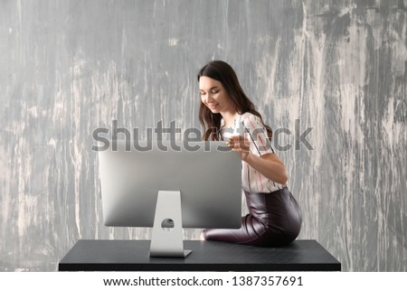 Beautiful young woman with computer sitting on table against grey background