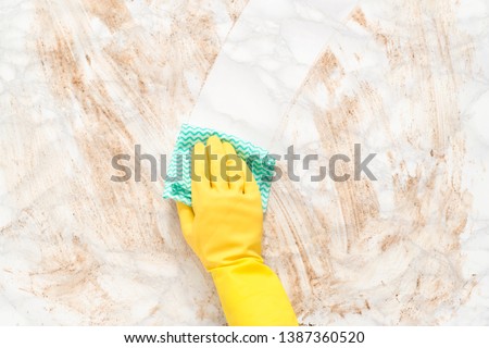 Hand wearing a glove, wiping clean a dirty marble counter or floor with a paper towel Royalty-Free Stock Photo #1387360520