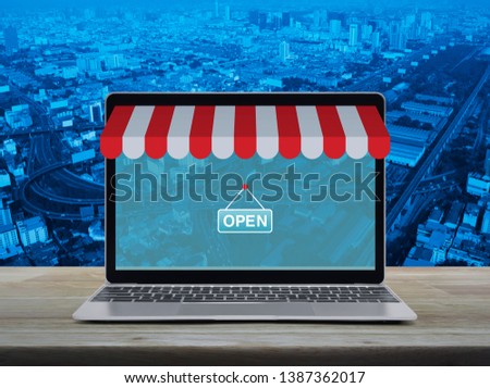 Modern laptop computer with online shopping store graphic and open sign on wooden table over city tower, street, expressway and skyscraper, Business internet shop online concept