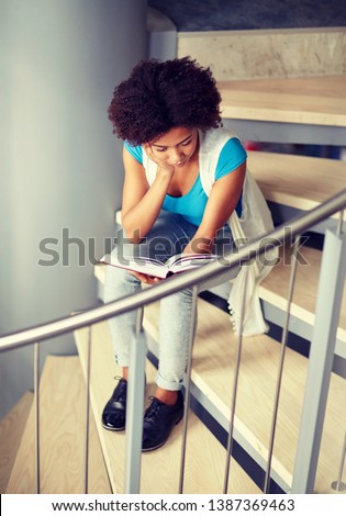 education, high school, university, learning and people concept - african american student girl reading book sitting on stairs at library