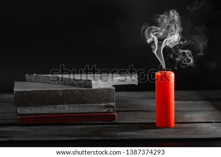 Closeup red candle smoke flowing on black background, pile of books on the old wooden floor and black background, 