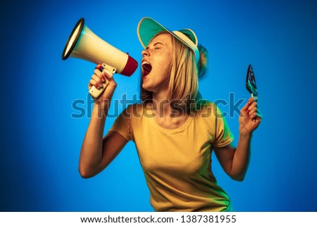 Beautiful female half-length portrait isolated on blue neon lights studio background. Woman in green cap with watermelon candy and mouthpiece. Facial expression, summer, weekend concept. Trendy colors