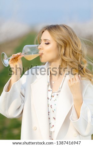 Beautiful blond girl drink juice from a glass outdoor in blossoming garden. Girl tastes juice. apple juice in glass. peach juice in glass. healthy lifestyle concept. spring concept. gorgeous blond