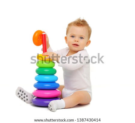 Baby 11 months in white clothes sitting on a white background and playing with a bright colored toy-pyramid