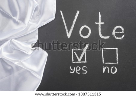 top view of white vote lettering and check mark near yes word on black chalkboard near white flag