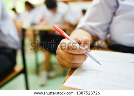 Student in uniform holding a pen taking final test in examination room, in collage or university classroom - education concept image of learner at the training center for professional development