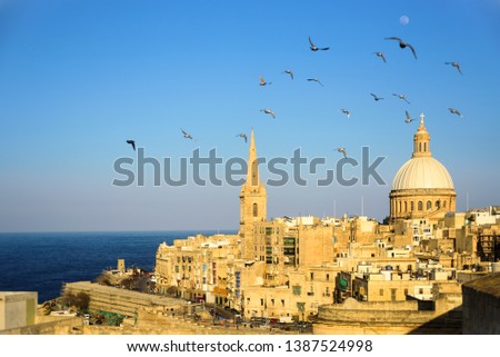 Classic postcard view to Basilica of Our Lady of Mount Carmel and St Paul's Pro-Cathedral. Valletta, Malta. Clear sky, sunshine, flying birds