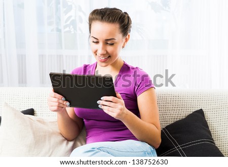 Smiling Brunette girl with dark tablet pc on the sofa
