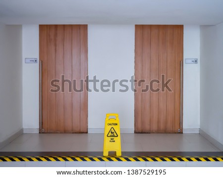 Yellow plastic signage, Wet floor warning signage stand in front of public toilet wooden entrance door, Male and female toilet, with yellow black warning strip on walk way for beware difference step.