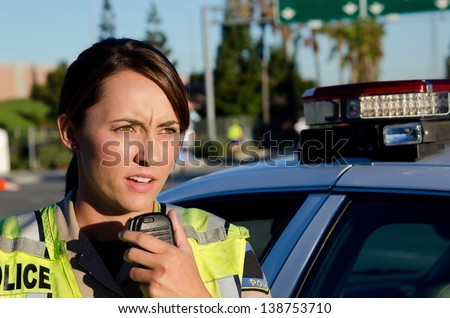 A female police officer standing next to her car about to talk on the radio. Royalty-Free Stock Photo #138753710