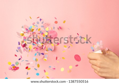 Colorful confetti in women's hands on pastel pink background. Bright and festive holiday background.