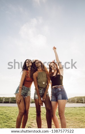 Excited young women standing outdoors with puckered lips and hand raised. Carefree girls in casuals posing outdoors for a picture.