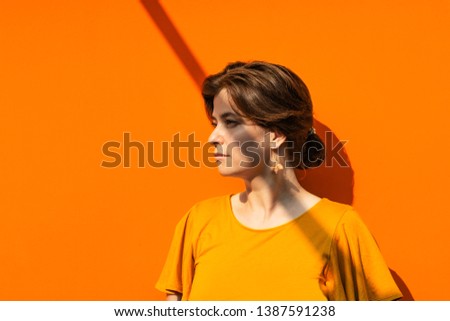 Beautiful young woman portrait in yellow blouse with linear shadow on her face and body. Orange metal background. Sunny day with high contrasts. Outdoor activities. 