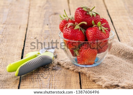 Red ripe strawberries in glass bowl on sackcloth and pruner on old wooden background.