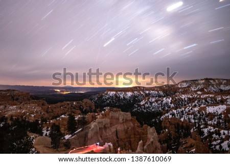 Star trails streaking across the night sky over a snow covered desert landscape. Bryce Canyon National Park's hoodoos and rock formations. 