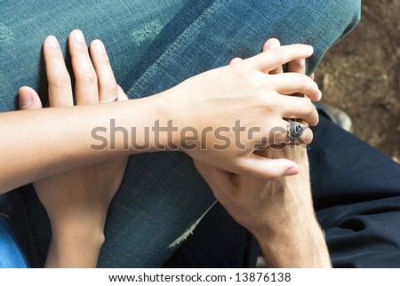 Close up of a couple's hands clasped together on their laps. Horizontally framed photograph.