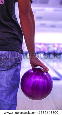 A boy holding a purple bowling ball at the bowling alley get ready to strike. This sport or game is call ten-pins bowling.