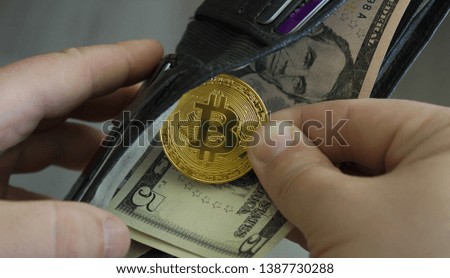 Hand pulls a bitcoin coin from a black wallet with dollar bills