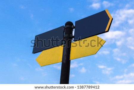 Yellow direction sign on the pole against the blue sky. Yellow arrow signal against sky.