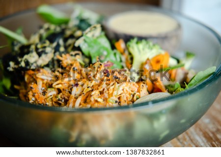 Vegan salad with various veggies and greens, and dressing in a glass bowl on a wooden table. Closeup, food blog, healthy eating, recipe