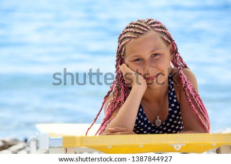 Portrait of preteen Caucasian girl with pink dreadlocks hairstyle tanning on beach on seacoast