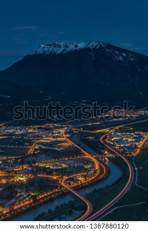 Night view of the city of Trento, Italy with snow capped mountain in background. Night view of a city between mountains and river. High dynamic picture of a city at night with snow capped mountain