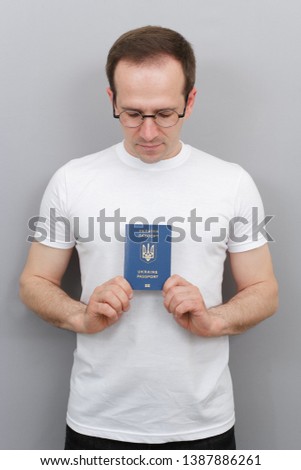 European man with a Ukrainian passport in his hands, wearing glasses, wearing a white T-shirt, a citizen of the country with a passport, studio photo with a man