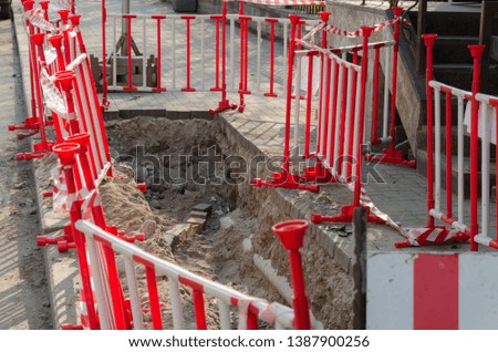 Dangerous pit on the sidewalk surrounded by warning red-and-white barriers. Repair of paving slabs.