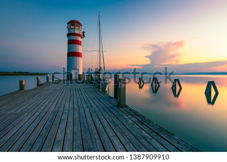 Lighthouse at Lake Neusiedl, Podersdorf am See, Burgenland, Austria. Lighthouse at sunset in Austria. Wooden pier with lighthouse in Podersdorf on lake Neusiedl in Austria. Royalty-Free Stock Photo #1387909910