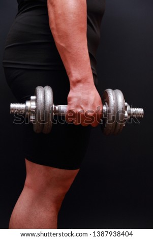 Closeup of  arm attractive athletic man with dumbbell on dark background.