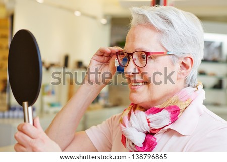 Happy senior woman with new glasses looking in mirror at optician Royalty-Free Stock Photo #138796865