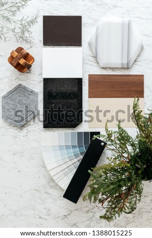 Top view of Material Selections including Granite tile, Marble tile, Acoustic tile, Walnut and Ash Wood Laminate and Painted color swatch with plant and flowers on marble top table. Royalty-Free Stock Photo #1388015225