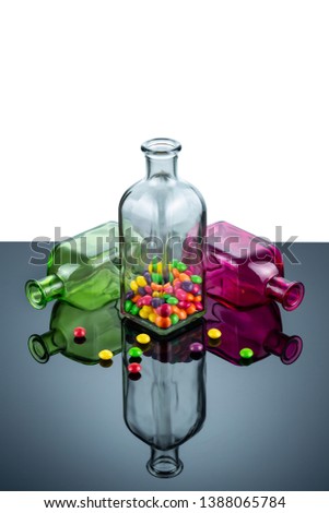 Bottles of rectangular shape made of colored glass filled with sweets are reflected in the mirror surface. Abstract bright color image.