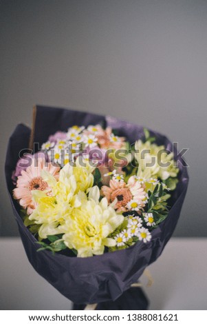 Close-up of a bouquet of colorful flowers in purple packaging stands on a white table on a blurred gray background
