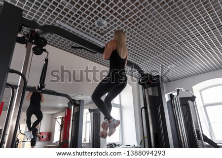 Athletic young woman with a beautiful body in black clothes in sneakers hangs on a modern simulator in the sport class. Girl trains in the gym.