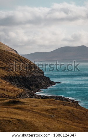Coastal cliffs with turquoise Atlantic water near the small village of Norðradalur on a windy spring afternoon (Faroe Islands, Denmark, Europe)