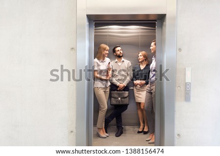 Colleagues talking while standing in elevator at office Royalty-Free Stock Photo #1388156474